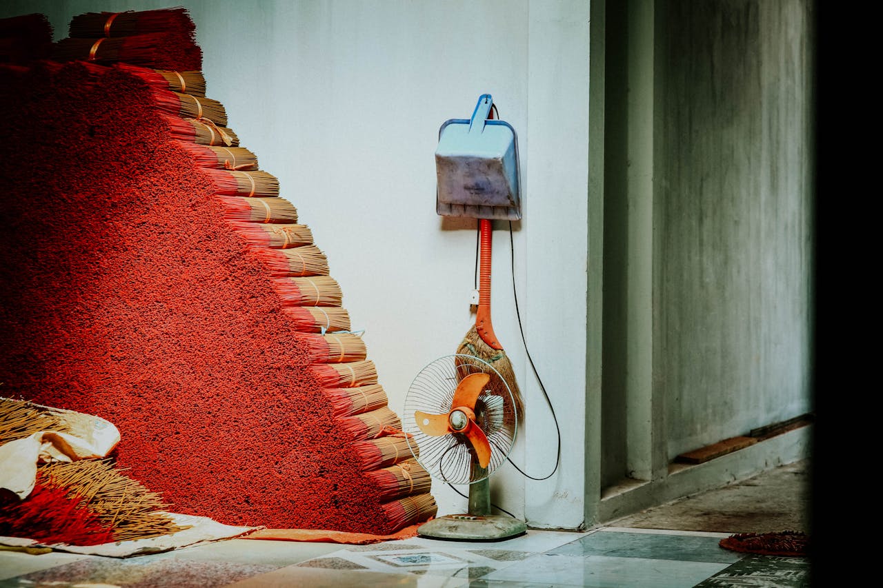 Service Close-up of stacked red broom bundles alongside a wall with a fan and cleaner.